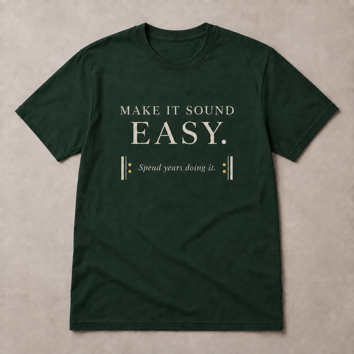 Make It Sound Easy Minimal T-Shirt in Forest Green with ivory A2 lettering and gold musical repeat dots, front view on a neutral background.