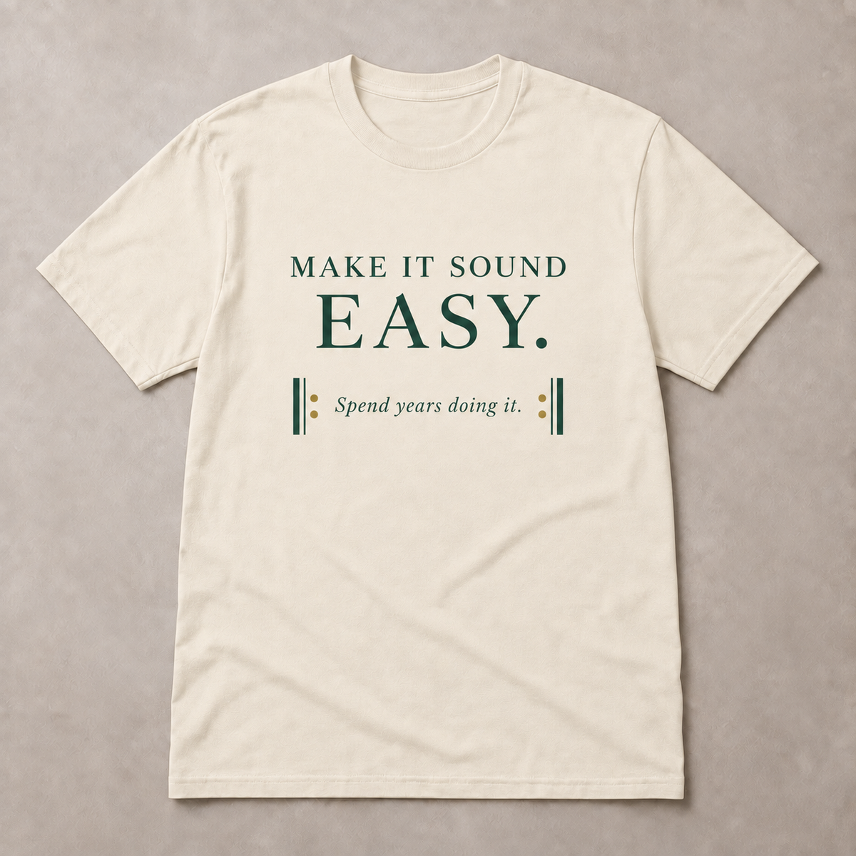 Make It Sound Easy Minimal T-Shirt in Warm Ivory with forest-green A2 lettering and gold musical repeat dots, front view on a neutral background.